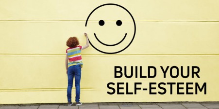 "Person drawing a large smiling face on a yellow wall next to the words 'Build Your Self-Esteem' — symbolising personal growth and self-confidence."